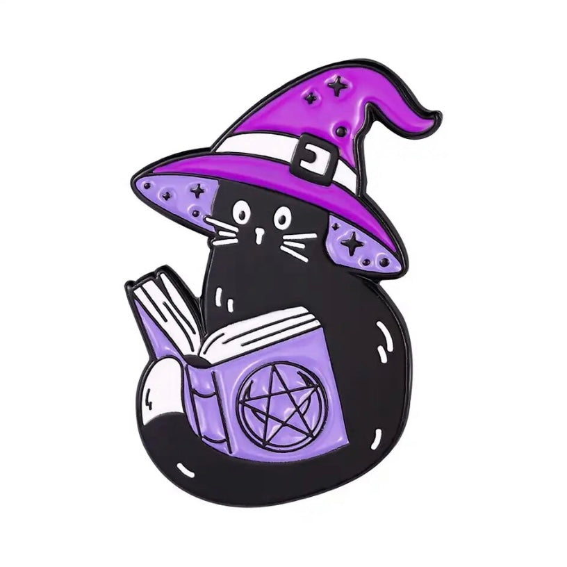 A meowgical enamel pin badge with a cute kitty in witch hat reading spells from a book :) purple and black colours.