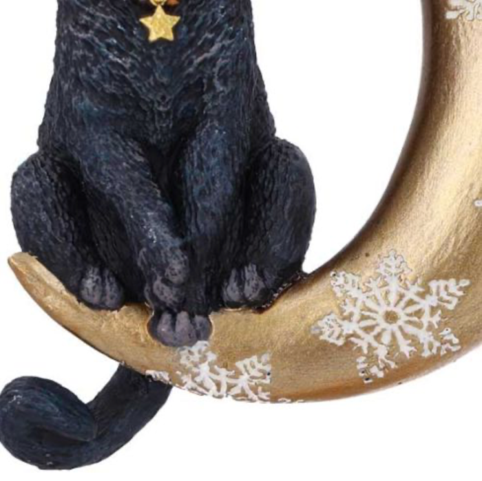 Black cat sitting on a golden crescent moon Christmas hanging ornament with white snowflakes closeup