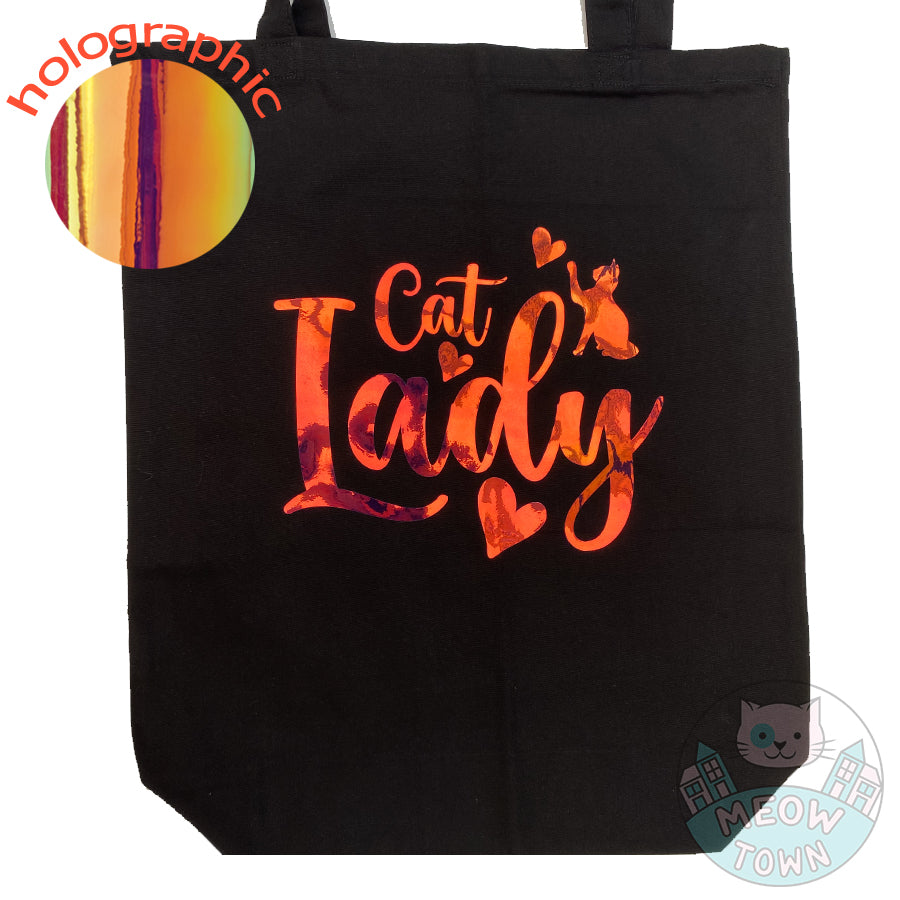 Meow Town Special, designed and printed in the UK by our team exclusively for You. Lovely Cat Lady slogan with kitty and hearts design with holographic vinyl print. Holographic print changes colour when looked from different angle, such as yellow/orange/green,etc. 100% cotton heavy duty black canvas tote bag.Purrrfect bag for any occasions all year round. It can also be a beautiful gift idea for the cat lover in your life.